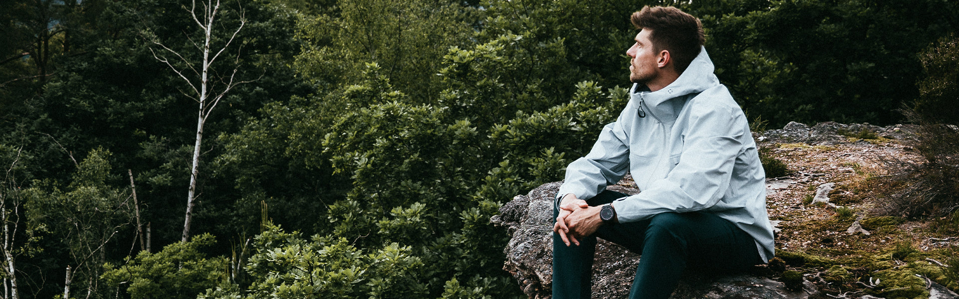 Person sitting on a rock in a forest wearing a light-colored jacket.